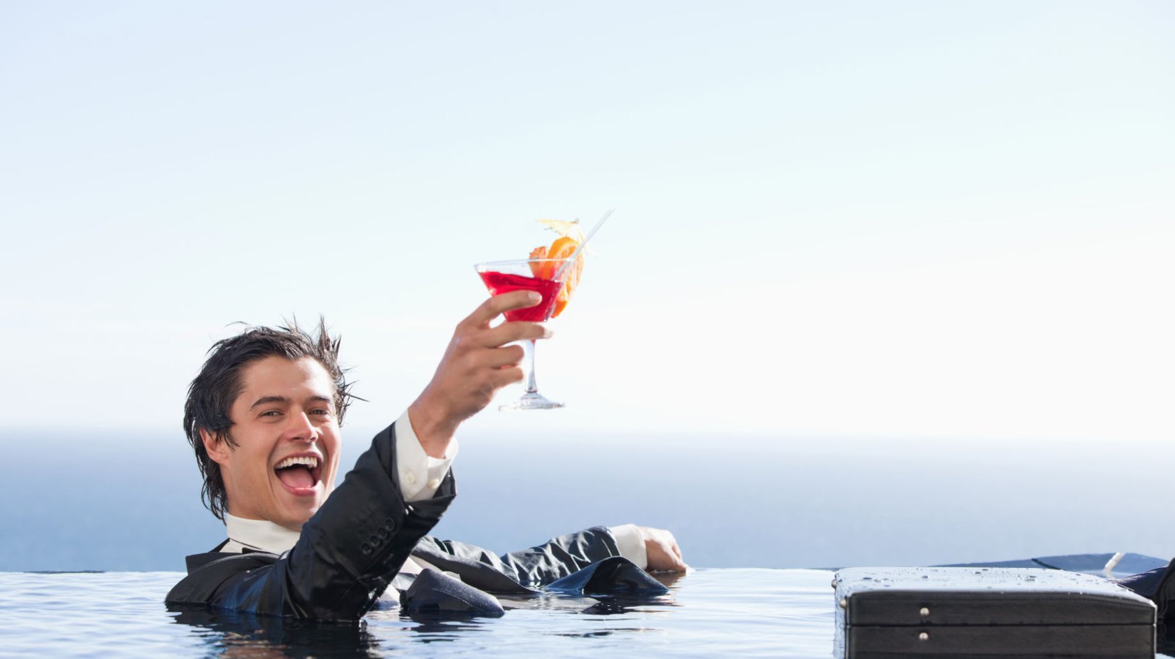 Fully clothed businessman in swimming pool holding cocktail